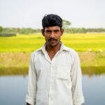 A portrait of a man standing near a pond in a rural countryside setting during summer.